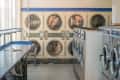 Laundromat interior with rows of front-loading washers, dryers, and a blue folding table.
