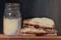 Peanut butter and jelly sandwich next to a mason jar filled with milk.