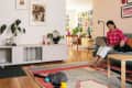 Woman in pink polka dot shirt on sofa with laptop, petting a rabbit; modern living room with plants and colorful decor.