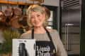 Woman in kitchen holding a box labeled "Dismembered Moments" with a black candle on a wooden board.