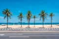 Palm trees line a beach with colorful umbrellas and a volleyball net under a clear blue sky.