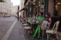 Three women sitting at a café table in Paris, wearing colorful outfits, with drinks and pastries on the table.