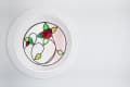 Round stained glass window with a red rose and green leaves design.