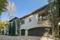 Two-story house with arched garage doors, wrought iron balcony, and tall trees in front.