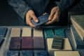 Person holding a blue rectangular tile among various colored tiles on a table.