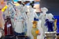 Porcelain figurines in traditional attire displayed among colorful vases at a market stall.