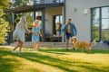 Family playing frisbee with a dog on a sunny lawn in front of a modern house.