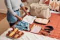 shot of folded clothes on a bed next to a duffle bag