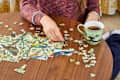 Close up view of woman in a multicolored sweater doing a puzzle on a wooden coffee table.