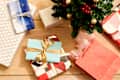 Overhead shot of an assortment of wrapped presents on a light wood surface, underneath a small decorated tree.