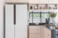 Modern kitchen with light wood cabinets, black countertop, white fridge, and open shelves with mugs and decor items.
