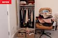 Wardrobe filled with hanging clothes, a chair piled with folded garments, and two woven baskets on the floor.