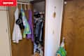 A cluttered closet with hanging clothes, jackets, and a basket on the floor, next to a wooden door.