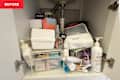 Cluttered bathroom cabinet filled with various skincare products, containers, and a pump bottle.