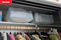 Storage bins on a shelf above a wooden clothing rod with various hanging garments in a closet.