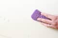 Hand cleaning a surface with a purple sponge, removing water droplets.
