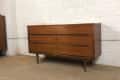 Mid-century modern wooden dresser with six drawers against a white brick wall.