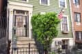 Green two-story townhouse with white trim, American flag, and potted plants on front steps.