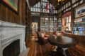 Library with wood-paneled walls, leather armchairs, a large bookshelf, ornate fireplace, and a hexagonal table.