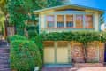 Two-story house with green trim, large windows, brick facade, and lush ivy-covered entrance.