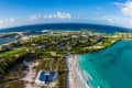 Aerial view of a coastal resort with sandy beaches, turquoise water, and lush greenery under a clear blue sky.