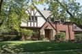 Tudor-style brick house with gabled roof, surrounded by trees and shrubs.