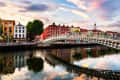 Ha'penny Bridge over River Liffey with colorful buildings and sunset sky in Dublin.
