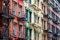 Colorful apartment buildings with fire escapes, featuring red, green, and beige facades.