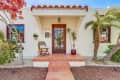 Spanish-style house entrance with terracotta tiles, wooden chair, potted plants, and arched doorway.