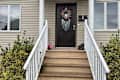 Front entrance with a dark door, decorative wreath, white railings, and potted flowers beside the steps.