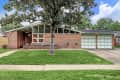 Mid-century modern brick house with large windows, green lawn, and a two-car garage.