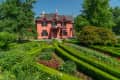 Historic red Gothic Revival house with ornate trim, surrounded by lush formal gardens and manicured hedges.