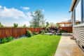 Backyard with green lawn, wooden fence, patio furniture, and large umbrella.