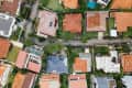Aerial view of suburban neighborhood with houses featuring red and blue roofs, green lawns, and a swimming pool.