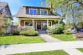 Two-story craftsman house with a covered porch, surrounded by lush greenery and a well-maintained lawn.