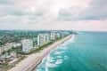 Aerial view of beachfront high-rise buildings along a coastline with waves and cloudy sky.