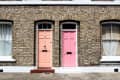 Two adjacent brick house entrances with a peach door on the left and a pink door on the right, each with arched windows above.