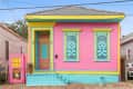 Colorful house with pink walls, turquoise shutters, yellow trim, and a pink door featuring a warning sign.
