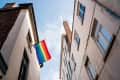 Rainbow flag hanging between two buildings against a blue sky.