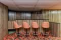 Basement bar with wood paneling, four brown swivel bar stools, and red patterned carpet.