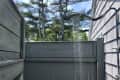 Outdoor shower with a modern showerhead, surrounded by wooden fencing and trees in the background.