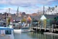 Fishing boats docked at a harbor with stacked lobster traps and colorful buildings in the background.