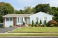 Single-story house with light blue siding, manicured lawn, shrubs, and pink flowers in front yard.