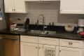 Kitchen sink with black countertop, white cabinets, dish rack, soap dispensers, and a bowl with sweet potatoes.