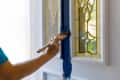 Painting a white door with blue paint next to stained glass panels.