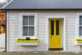 Gray house exterior with a bright yellow door and matching window boxes filled with plants.