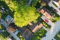 Aerial view of suburban neighborhood with tree-lined streets, parked cars, and houses with brown roofs.