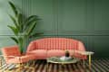 Coral sofa and chair with gold frames, green paneled wall, large plant, and marble coffee tables on checkered floor.