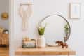 Wooden console table with round mirror, potted plant, woven basket, and decorative wooden rhino figures.