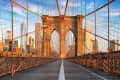 Brooklyn Bridge walkway with suspension cables, city skyline, and blue sky at sunset.